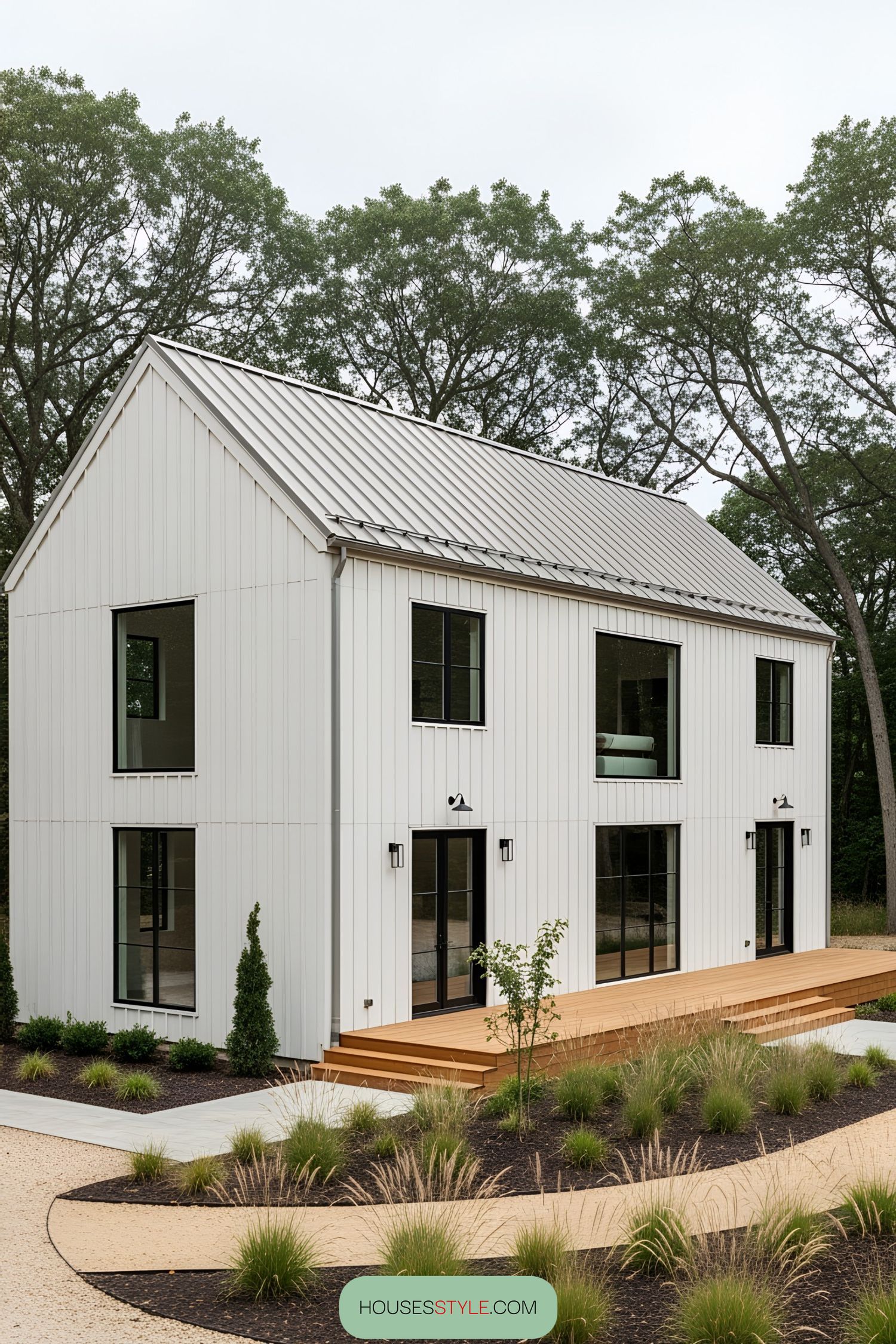 Modern white barn house surrounded by trees with a wooden deck and landscaped garden