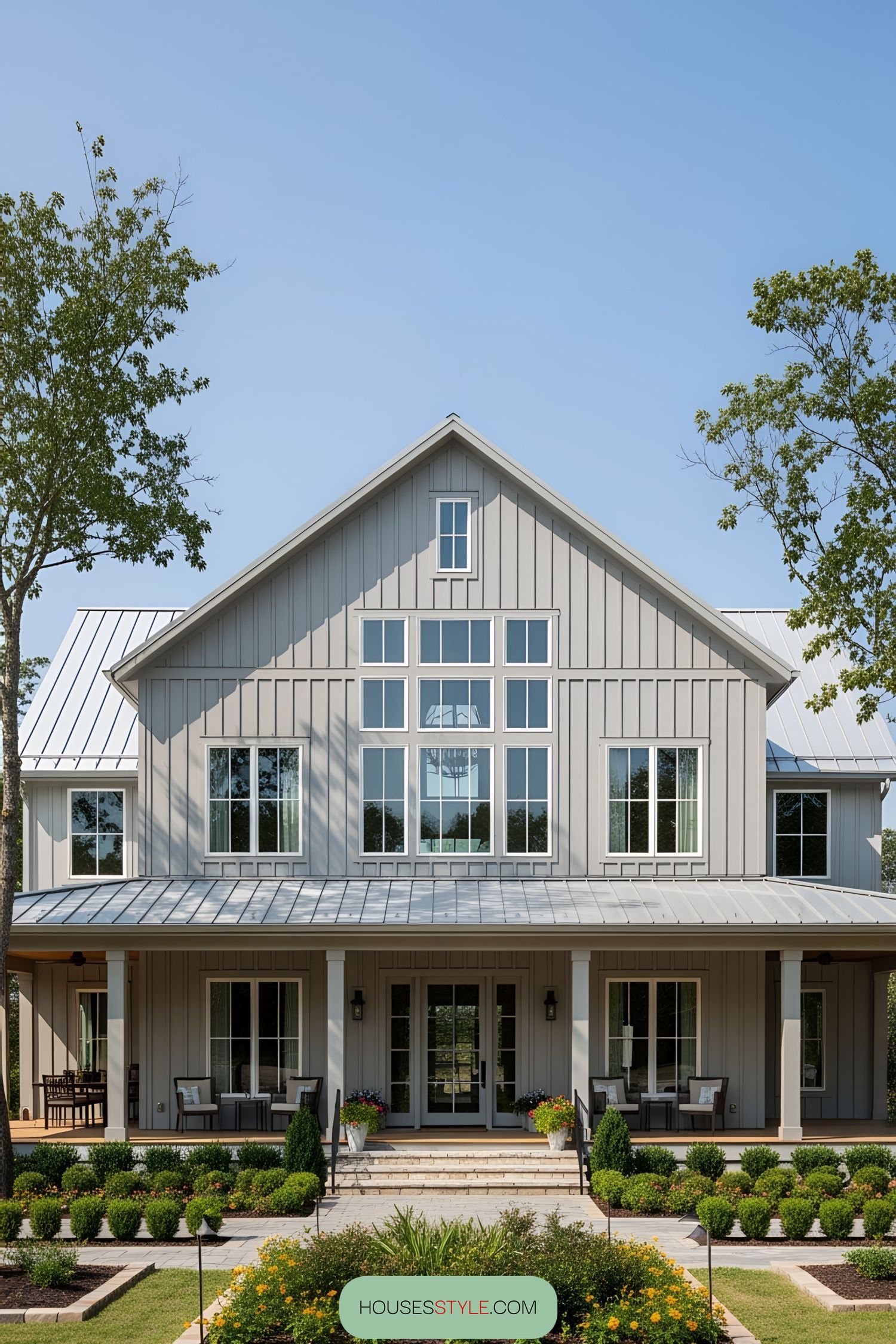 A gray barndominium with a wraparound porch and large windows