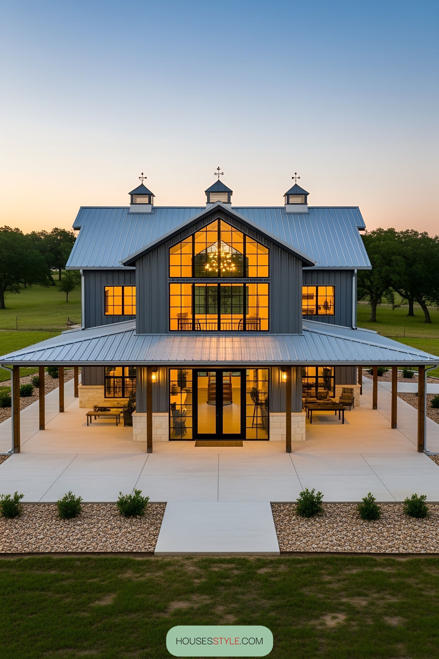 A modern barndominium with a wraparound porch at sunset
