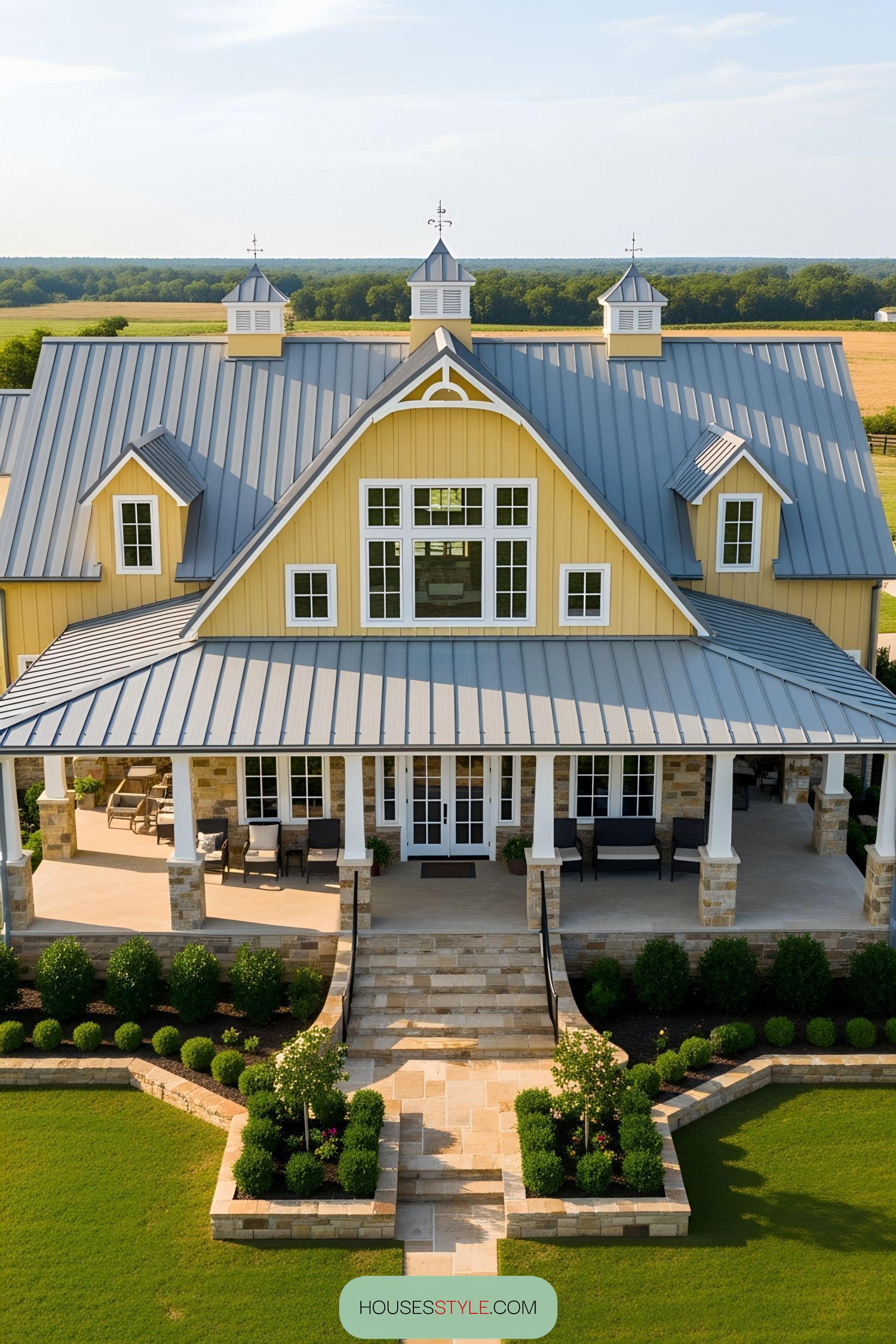 Yellow barndominium with large porch and green fields