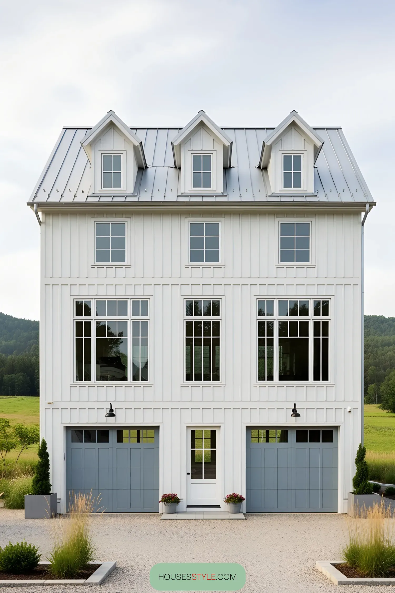 White farmhouse with blue garage doors and lush greenery
