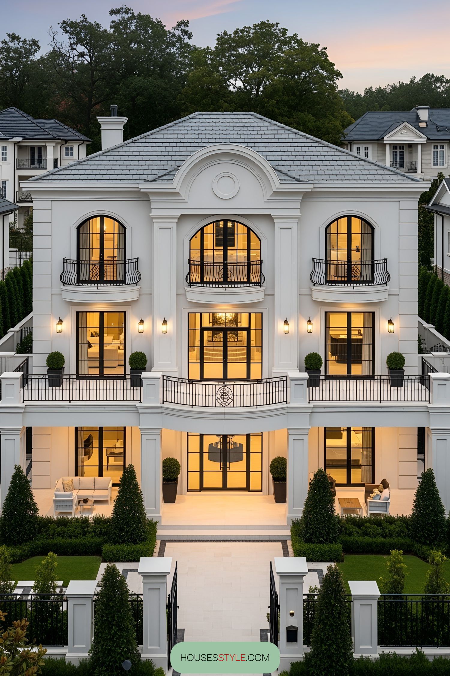 Luxurious three-story white villa with glowing windows and manicured gardens